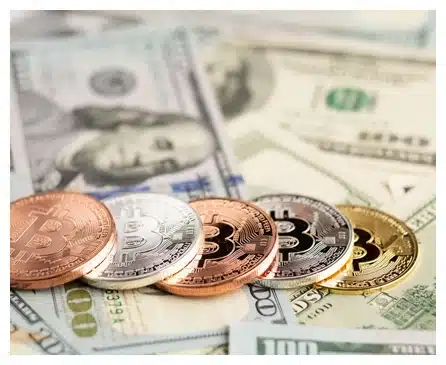 Several physical Bitcoin tokens in gold, silver, and copper colors are arranged in a row on top of scattered US dollar bills.