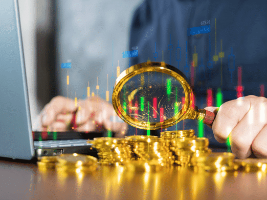 A person examines a stack of gold coins with a magnifying glass in front of a laptop, with colorful financial charts and graphs superimposed, symbolizing investment analysis and digital trading.