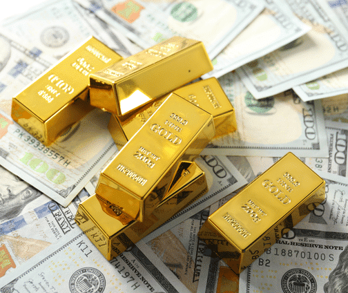 Several gold bars are stacked and scattered on top of a pile of U.S. hundred-dollar bills, symbolizing wealth and investment.