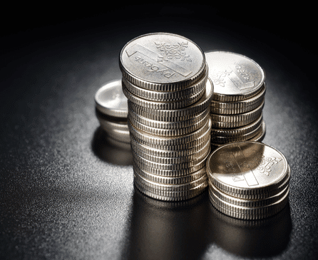 Stacks of shiny silver coins arranged on a dark, reflective surface, with light highlighting the embossed designs on the coins.