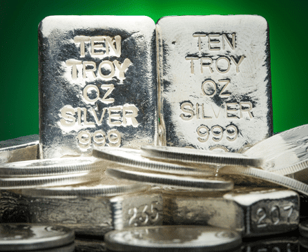 Two ten troy ounce silver bars marked “TEN TROY OZ SILVER 999” stand upright among several silver coins and bars, with a green gradient background.