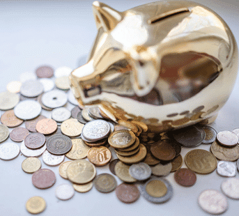 A golden piggy bank is surrounded by scattered coins of various currencies and denominations on a white surface.
